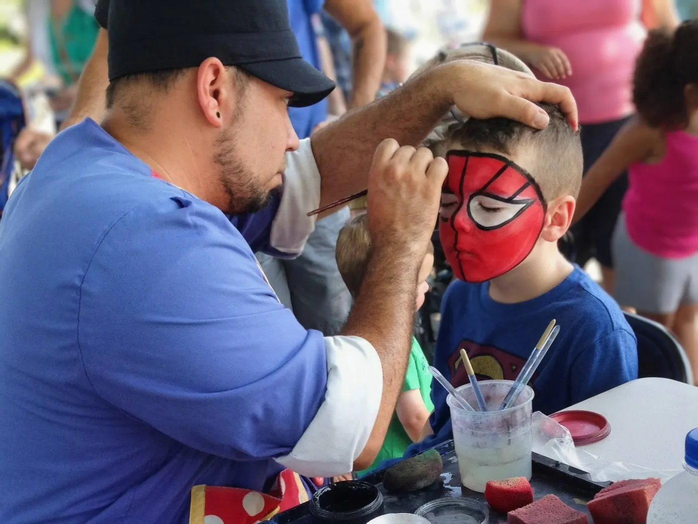 A performer painting a red mask design on a child